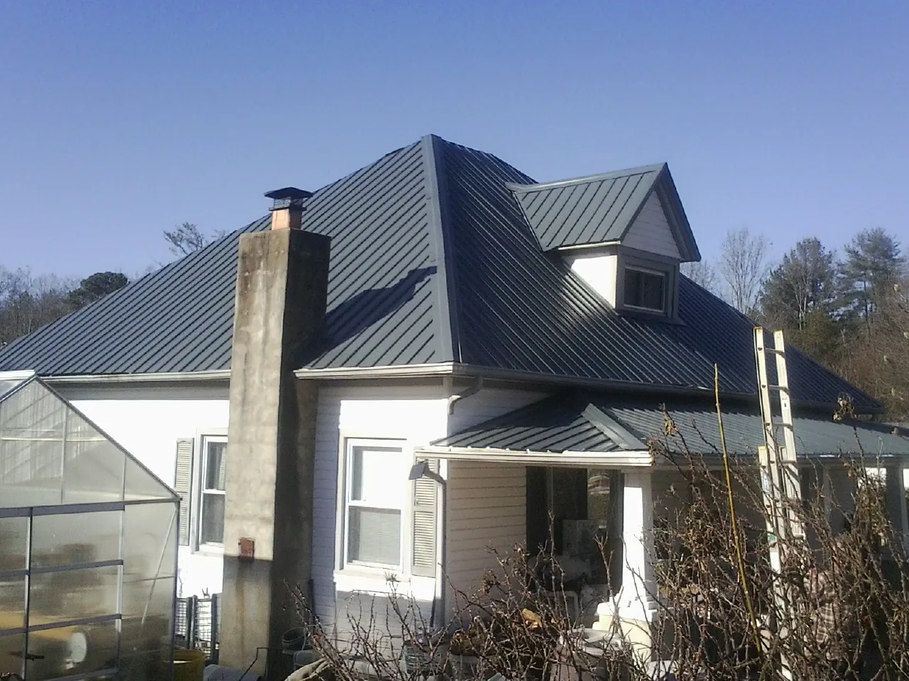 Dark blue standing seam metal roof on a white farmhouse with dormer — Slate & Tile Roof Repair by Roofing Brothers in Great Falls